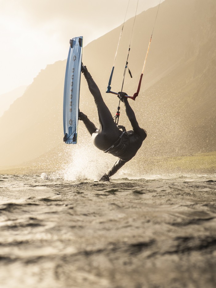 Kitesurfer en combinaison néoprène ION effectuant une figure dans les vagues