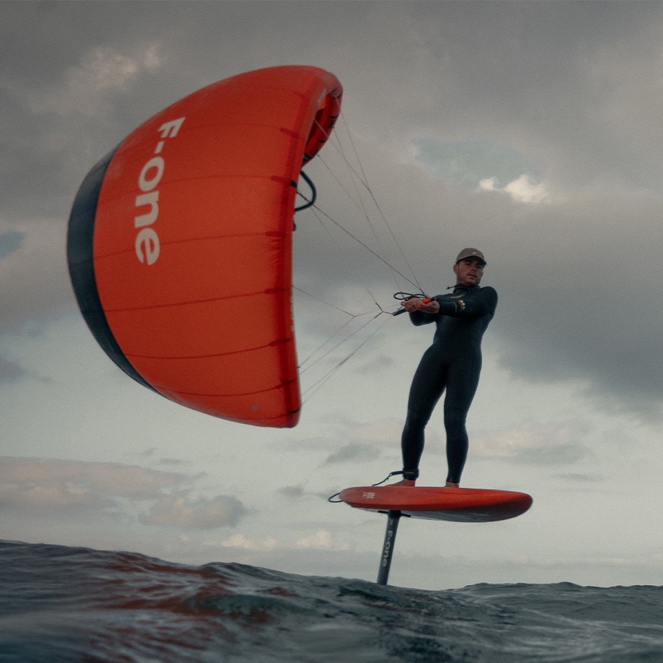 Rider en plein mouvement sur foil – maîtrise de l’aile en K-Wing sous un ciel menaçant